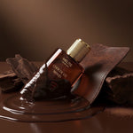 MELITE PARFUMS Chocolate Wood unisex perfume bottle with gold cap, surrounded by melted chocolate and dark wood.