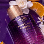 MELITE PARFUMS Intoxicating Femininity Florale perfume bottle with gold cap, surrounded by gardenia and orange slices.
